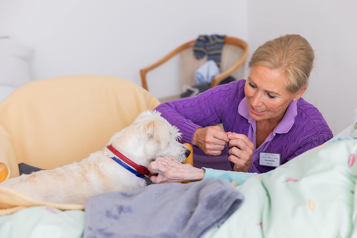 Pflegerin mit Therapiehund besucht eine Seniorin im Aschrottheim
